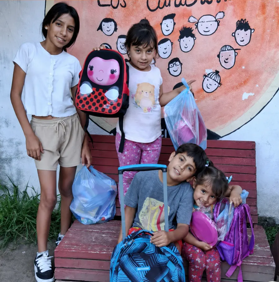 Cuatro chicos y chicas posan en un banco con las mochilas y los útiles escolares que acaban de recibir.