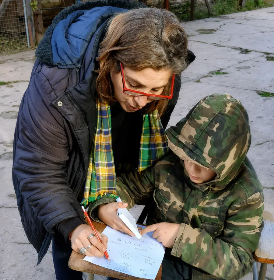Una voluntaria explica una cuenta a un nene, los dos inclinados sobre la hoja.