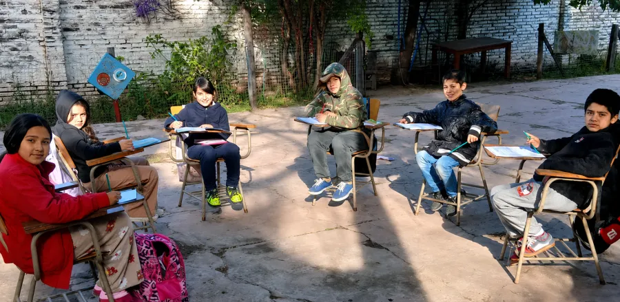 Chicos y chicas sentados en pupitres formando una ronda en el patio, haciendo la tarea.
