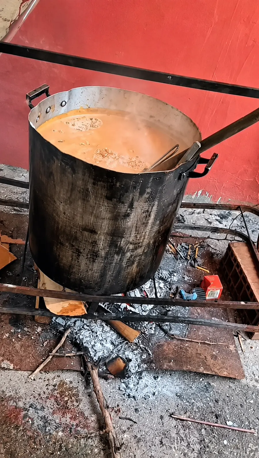 Una olla enorme con guiso humeante sobre el fuego a leña, contra la pared roja del comedor.