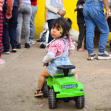 Nena chiquita sentada en un camioncito de juguete en el patio.