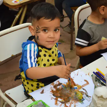 Nene con babero pintando con los dedos en la mesa del taller.