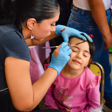 Nena de remera rosa con los ojos cerrados durante el maquillaje artístico.