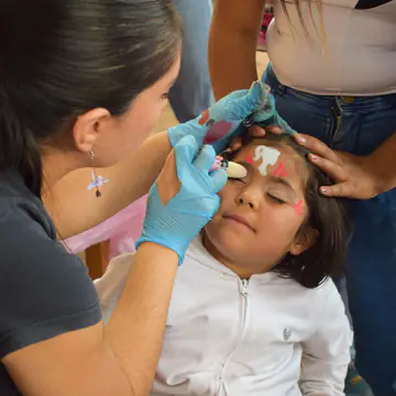 Una voluntaria pinta la cara de una nena que espera quieta.