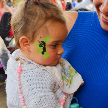 Nena chiquita con un collar de colores y la cara pintada.