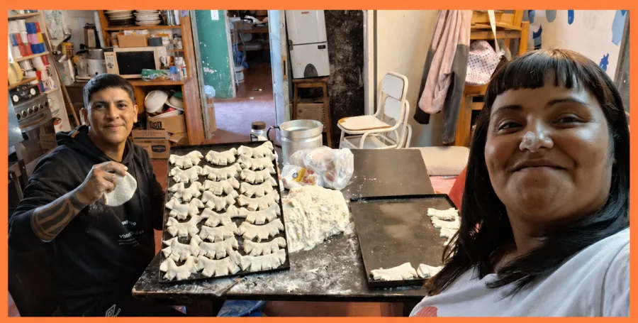 David y Mica en la cocina, con dos bandejas de empanadas armadas sobre la mesa.