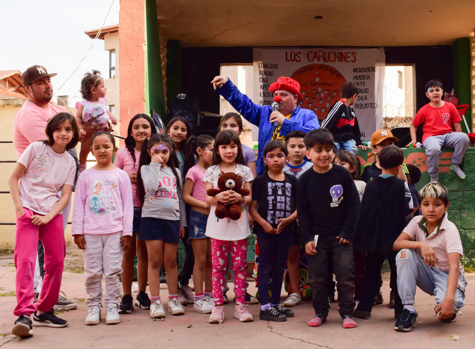 Un grupo grande de chicos y chicas posa en la entrada del comedor, algunos con los brazos levantados.