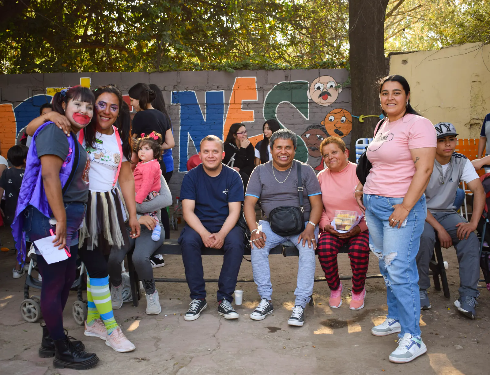 Familias sentadas frente a las letras gigantes que dicen Infancias, en el patio del espacio.