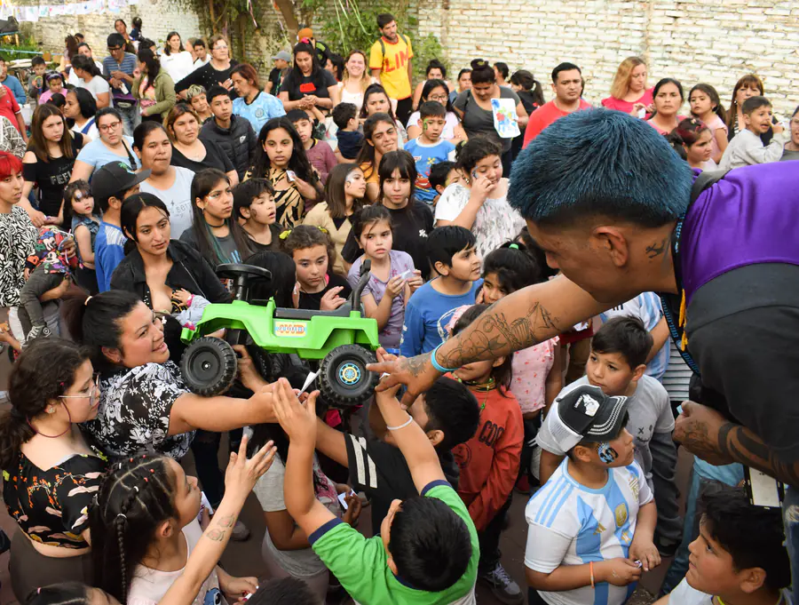 Un voluntario entrega juguetes a una multitud de chicos con las manos levantadas.