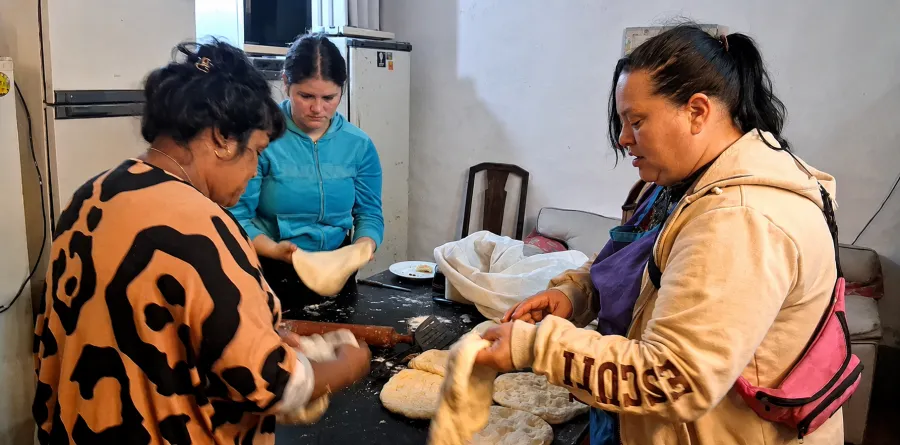 Tres mujeres estiran y arman la masa sobre la mesa de la panadería.