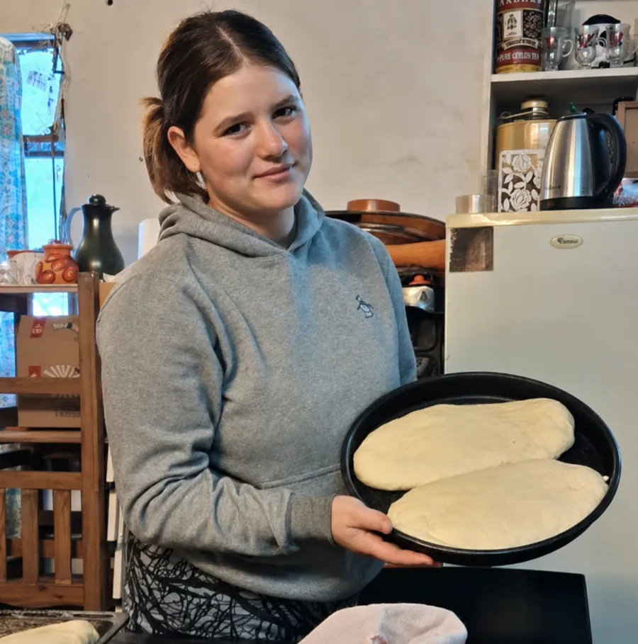 Una chica sostiene la bandeja con dos panes listos para entrar al horno.