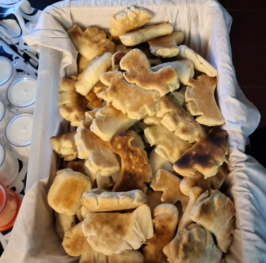 Manos preparan panes y sándwiches sobre una mesa larga durante una jornada del comedor.