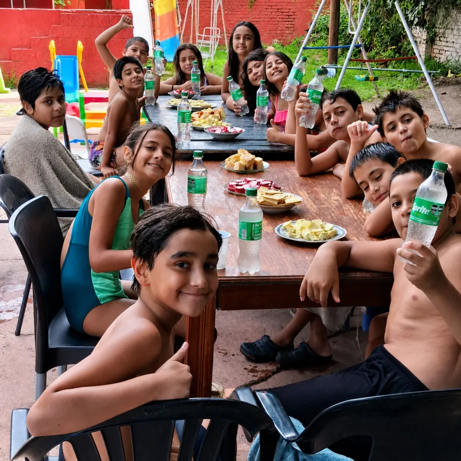 Una mesa larga llena de chicos y chicas en malla, comiendo y brindando después de la pileta.